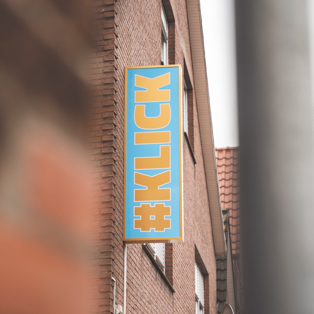 Leuchtreklame Schild von #KLICK am Bürogebäude. Das Schild ist Blau mit goldener Aufschrift (#KLICK)