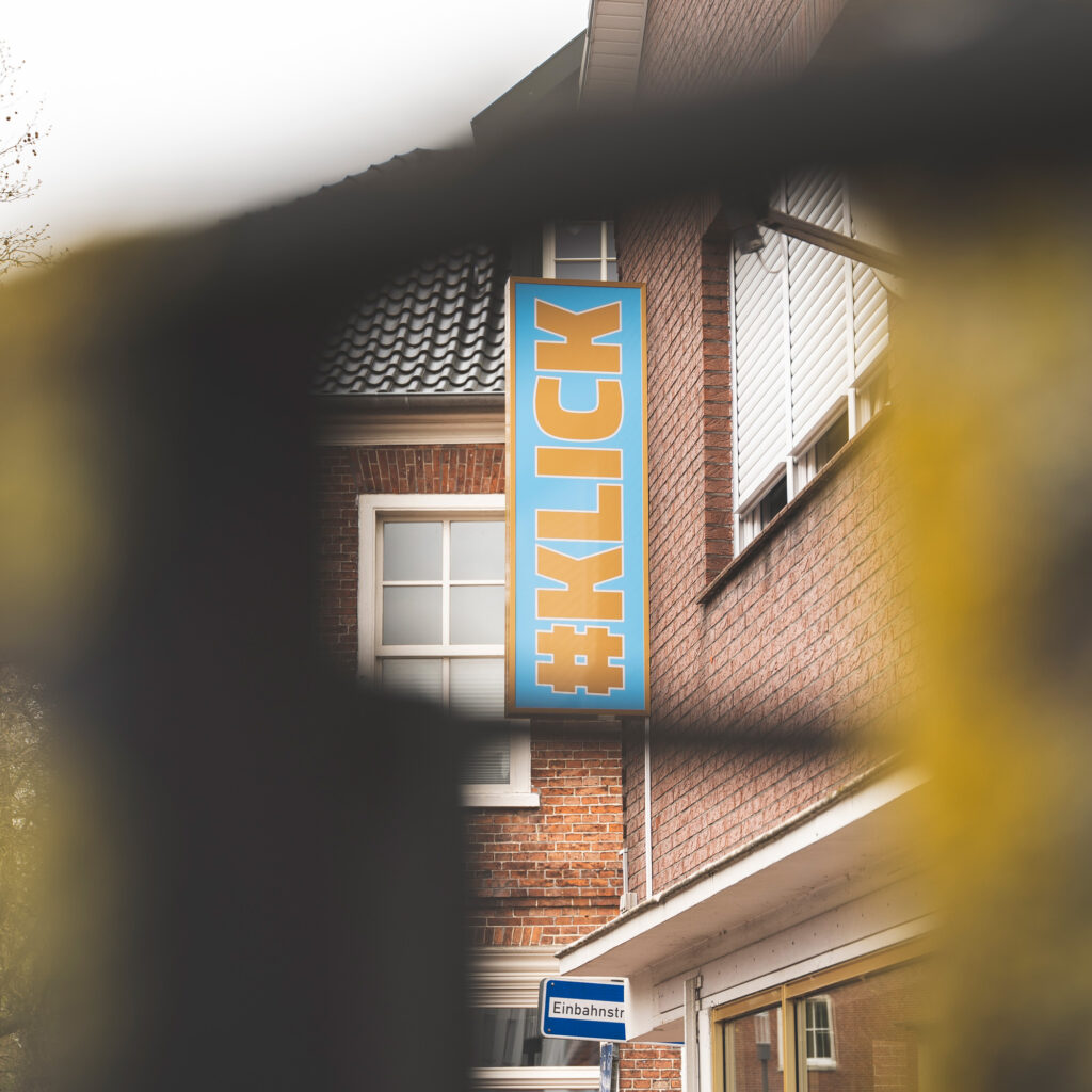Leuchtreklame Schild von #KLICK am Bürogebäude. Das Schild ist Blau mit goldener Aufschrift (#KLICK)